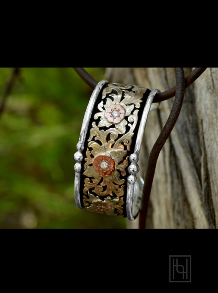 Classic Floral Cuff Bracelet hanging on tree - black background w/ yellow gold scrolls, green gold leaves, rose gold flower and crystal clear cz stones
