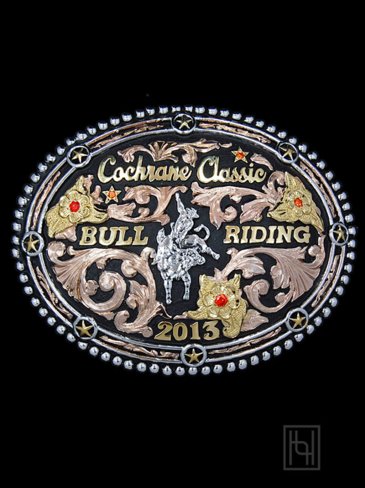 Black background w/ rose gold scrolls, yellow gold lettering and flowers, silver casted bull riding figure, sunset orange cz stones