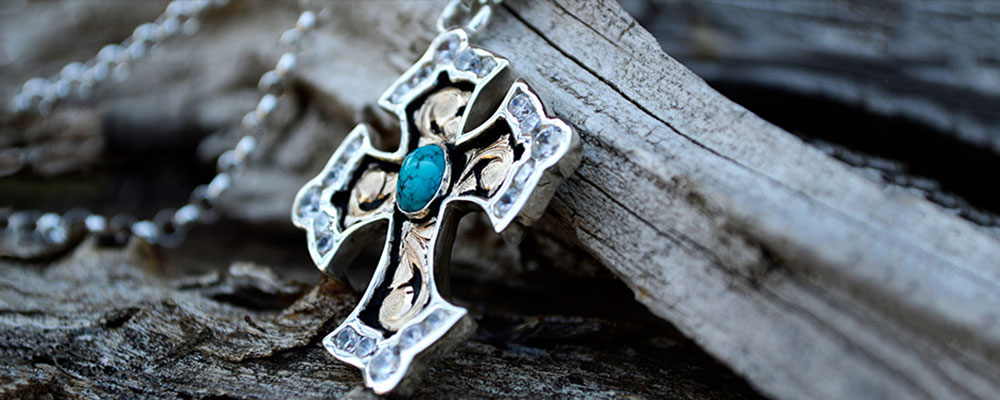 Lifestyle photo of silver cross pendant w/ black background and yellow gold scrolls, 8x6 oval blue turquoise stone, 3 & 4mm crystal clear cz in edge