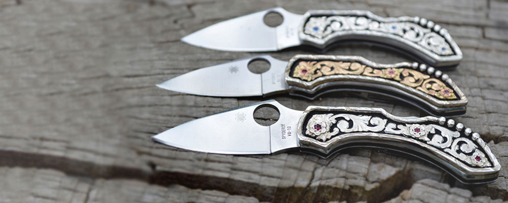Header for website - three stock knives w/ yellow gold scrolls and garnet cz stone and two knive with silver scrolls and sapphire blue cz and one with ruby red cz