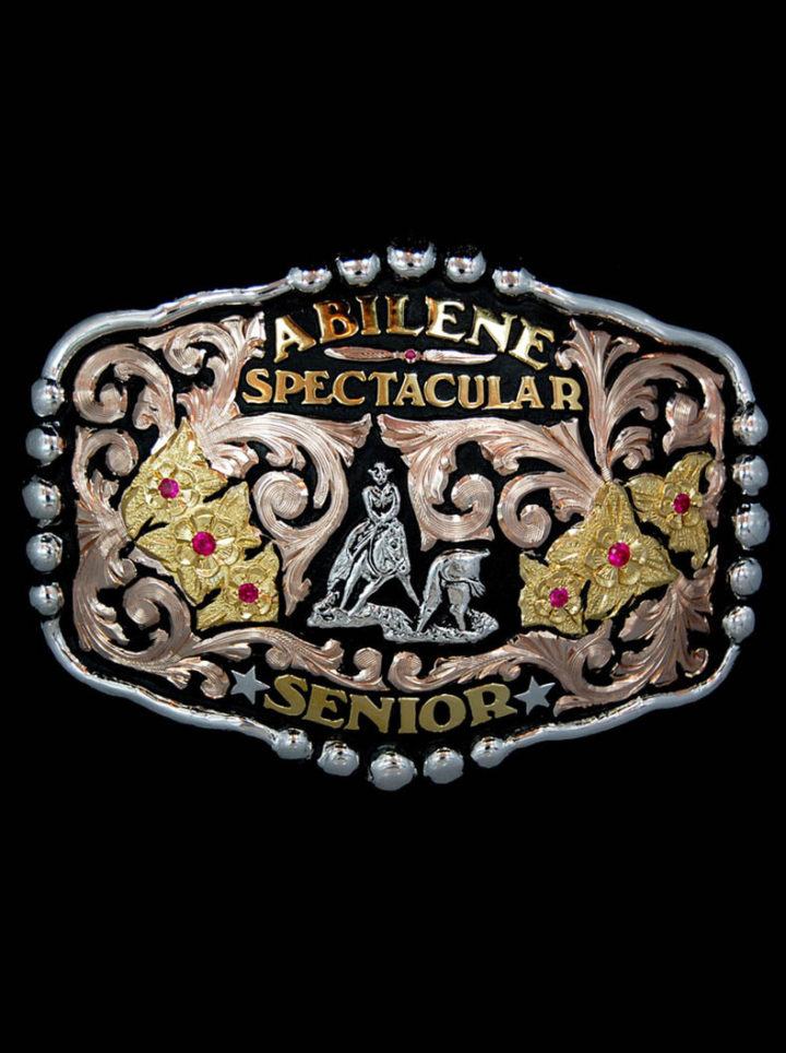 Wyoming Custom Buckle with black background and rose gold scrolls, yellow gold flowers and lettering, ruby red stones and silver calf roping figure